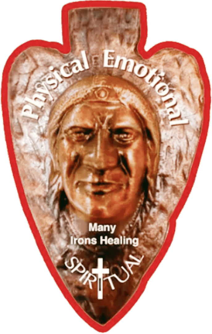 A stone carving of a face wearing a headdress, surrounded by the words "Physical Emotional Spiritual Many Irons Healing" with a cross symbol.